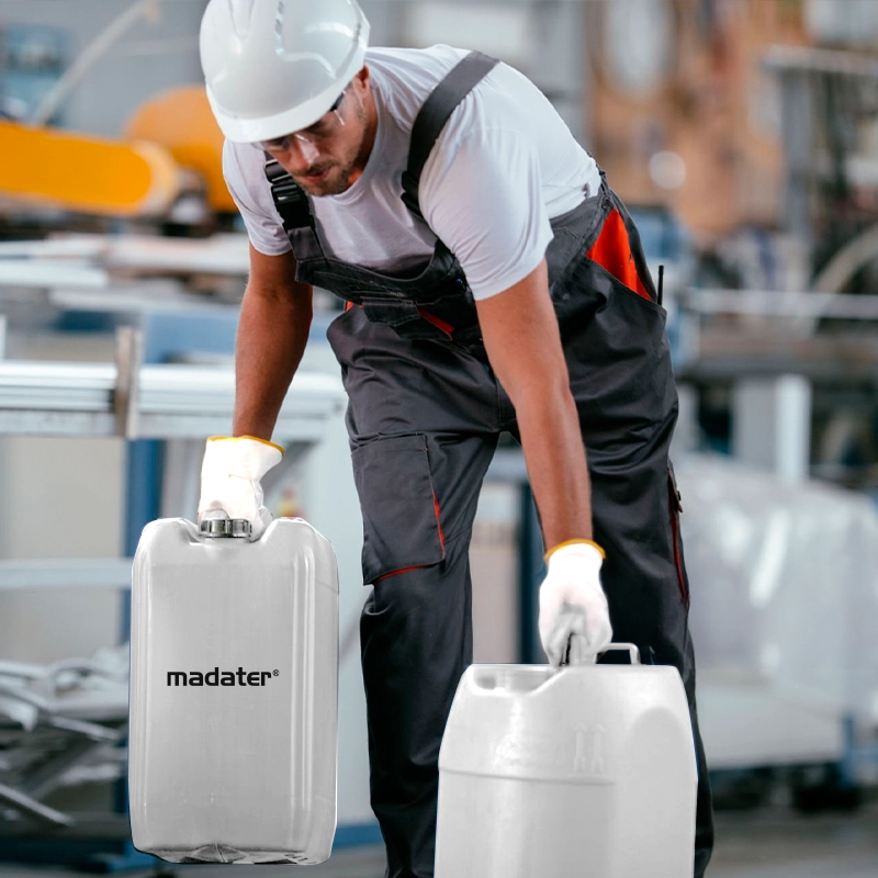 Homem usando capacete e uniforme de trabalho, com macacão de segurança, carregando dois galões de plástico com o logo Madater em uma fábrica.
