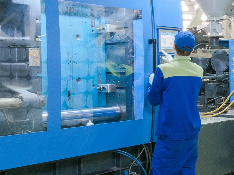 Operador manuseando painel de controle de uma injetora termoplástica azul em ambiente industrial, durante o processo de moldagem de peças plásticas na Madater.